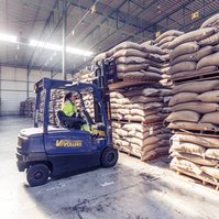 A woman in a forklift truck selects a bag of coffee in the warehouse
