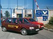 Two red cars in front of a gate. The cars have Berthold Vollers written on them and are therefore company cars. On a wall next to the gate, signs can be seen. They aren't completely clear readable, but it is obvious from them that we are at the Vollers location in Riga.
