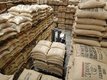 A coffee warehouse from inside. The photo is taken from an upper angle so that you can see the staples of bags from above. In the middle there's also a forklift that has multiple bags loaded.