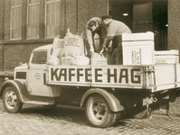 An old sepia photo of two people unloading coffee bags from a car