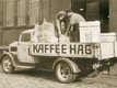 An old sepia photo of two people unloading coffee bags from a car