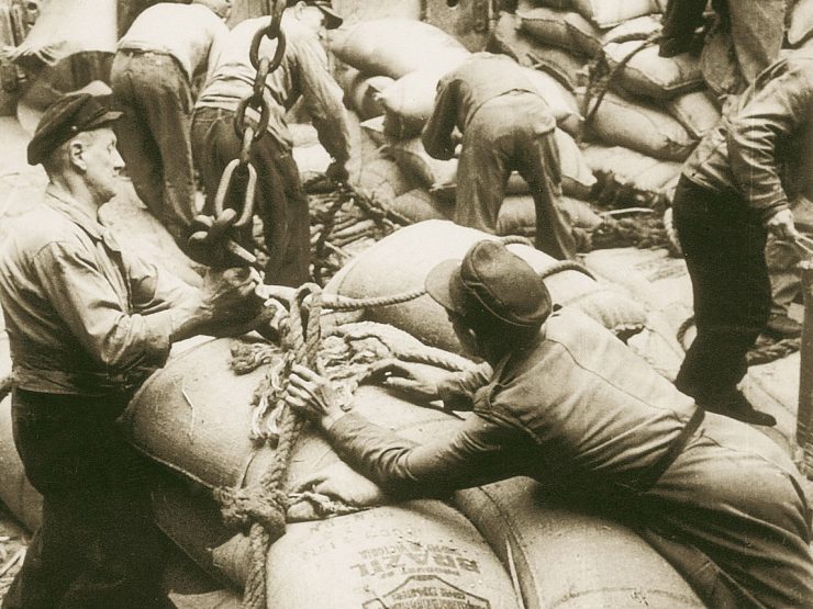 An old sepia photo of port workers with coffee bags, probably on a ship. It is unclear if they are loading or unloading the bags.
